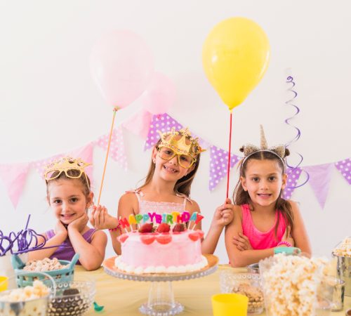 pretty-birthday-girl-with-her-friends-wearing-eye-mask-standing-variety-food-table